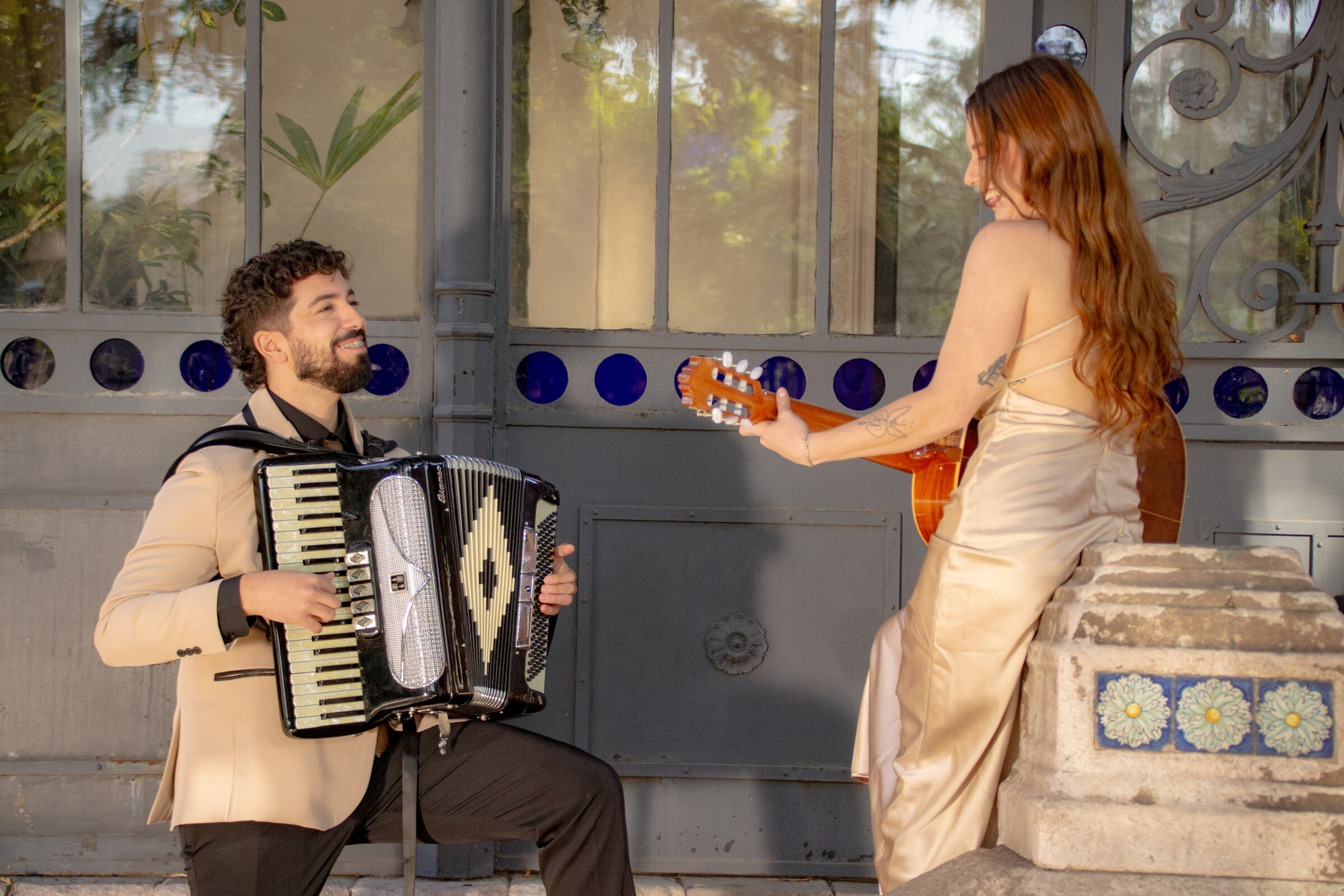 Dúo Amores de Chile tocando guitarra y acordeón, sonriendo con el Palacio Cousiño de fondo en Santiago.
