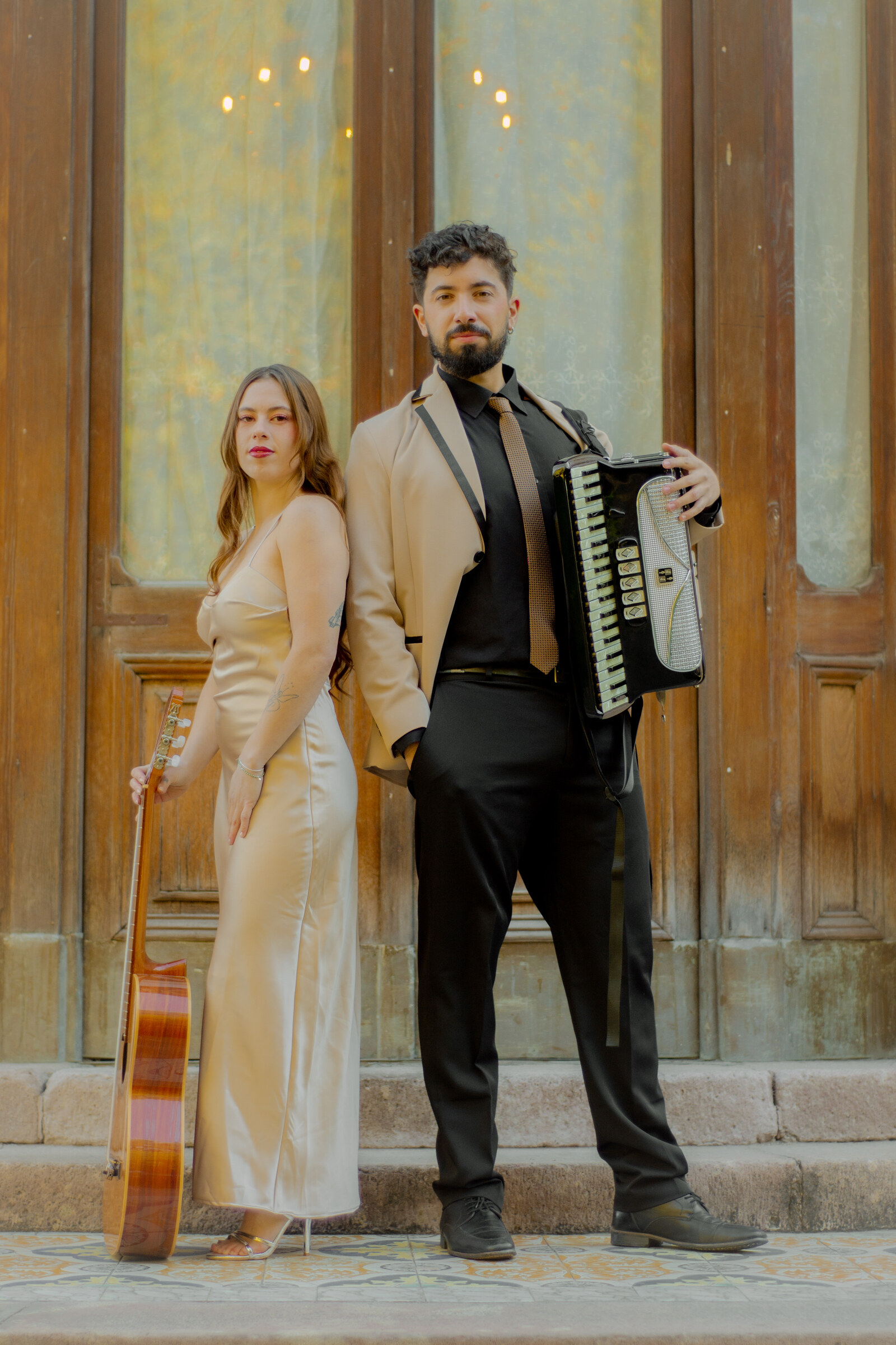 Dúo Amores de Chile posando elegante con guitarra y acordeón frente a puertas de madera del Palacio Cousiño.