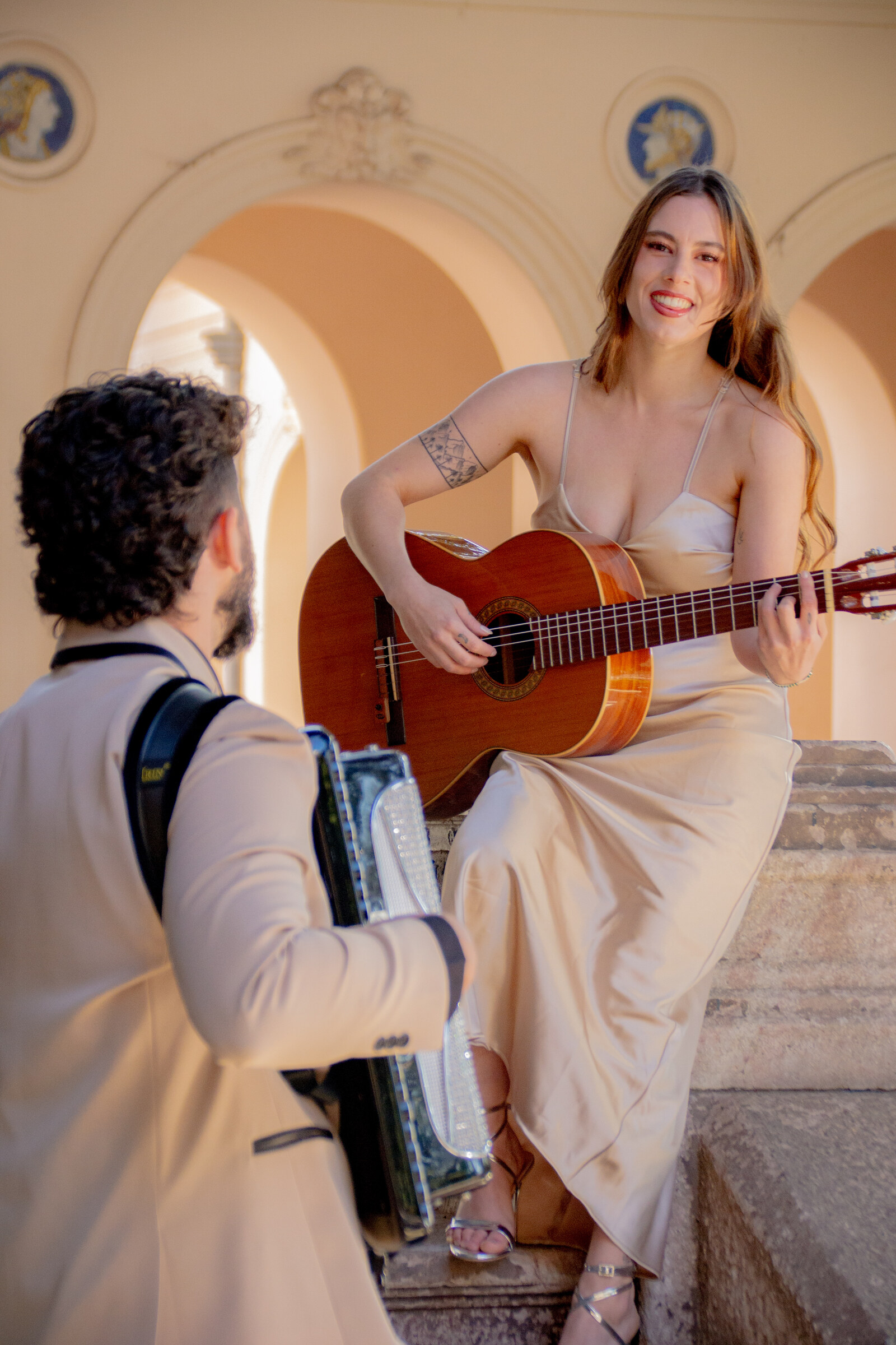 La cantante del Dúo Amores de Chile toca la guitarra y sonríe en el Palacio Cousiño, con su compañero de espaldas.