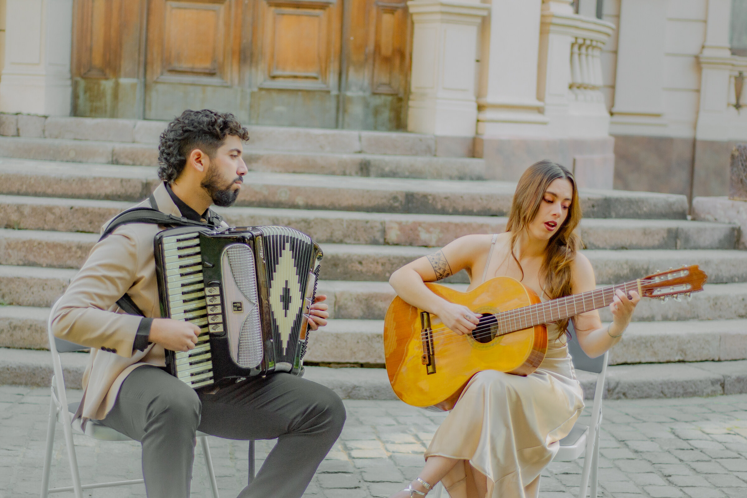 Dúo Amores de Chile tocando acordeón y guitarra frente a la imponente arquitectura del Palacio Cousiño.