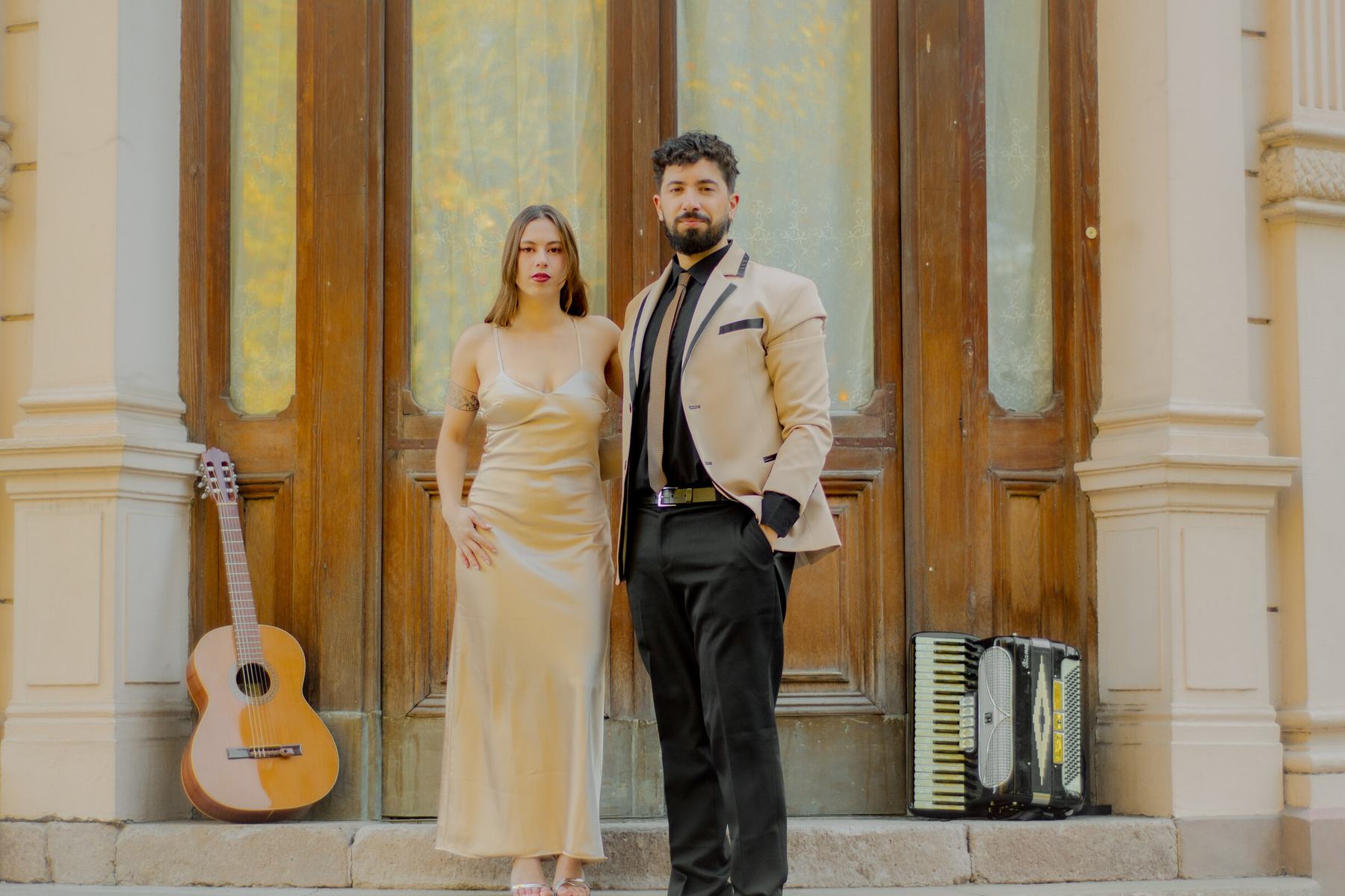 El Dúo Amores de Chile posa elegante con guitarra y acordeón frente a las puertas del Palacio Cousiño.